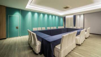 Une salle de conférence avec une longue table, des chaises blanches, des murs de couleur turquoise et un plancher en bois.