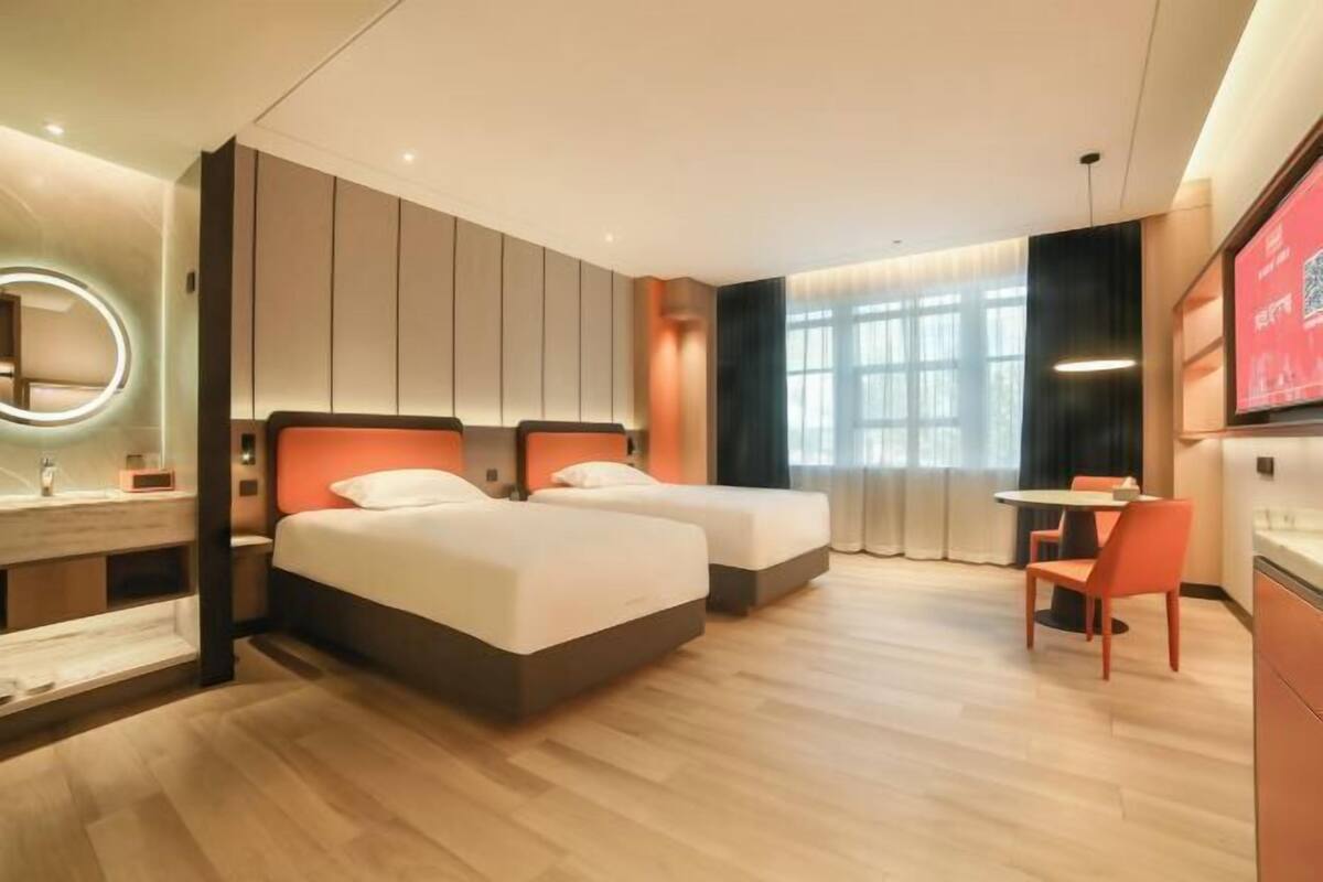 Ein Hotelzimmer mit zwei Betten, einem Schreibtisch, einem Stuhl, einem Spiegel und einem Fernseher.