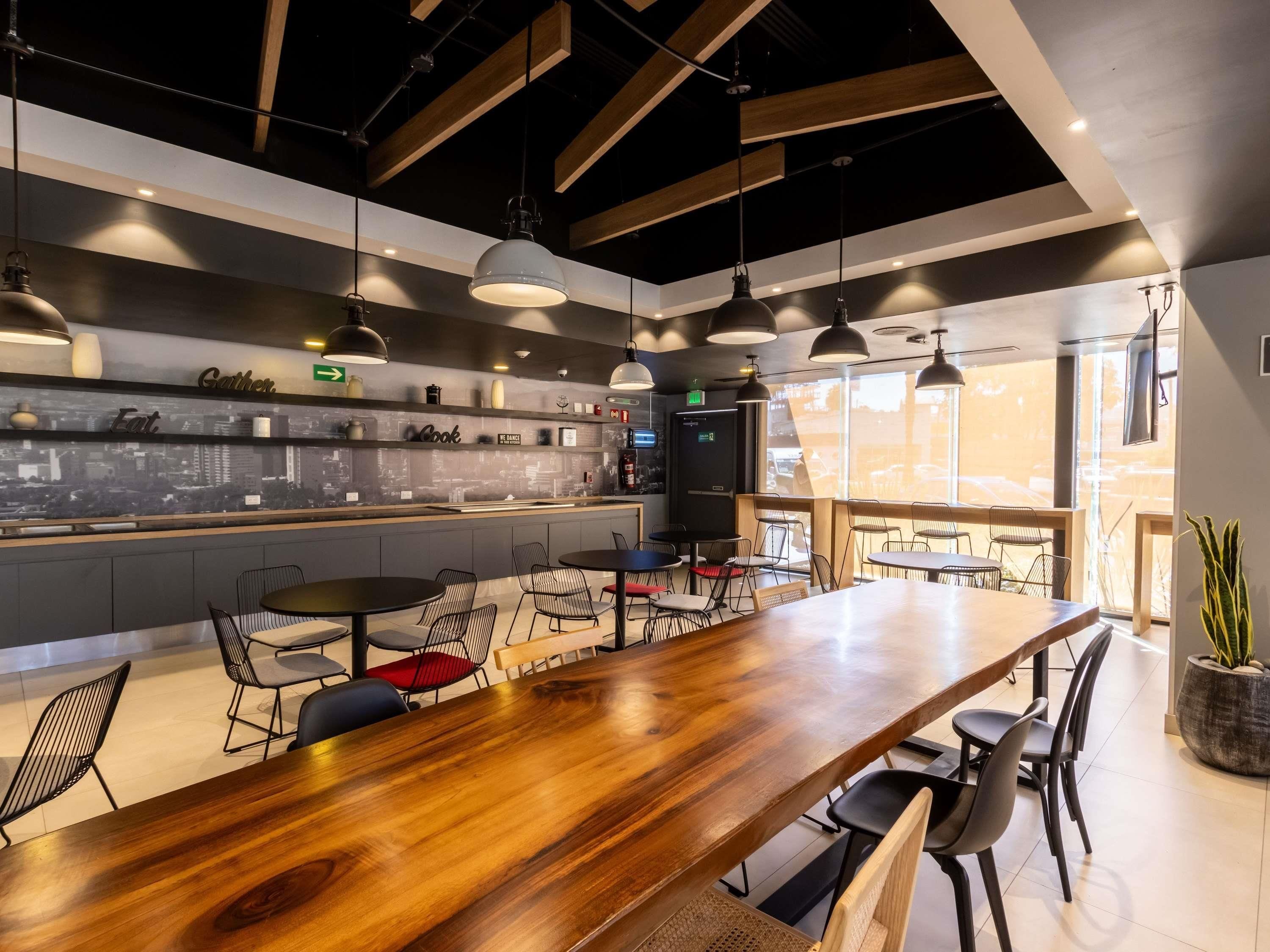 A modern restaurant with a long wooden bar, multiple seating areas, and a cityscape view through the windows.