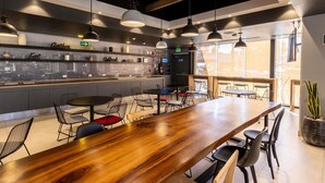 A modern restaurant with a long wooden bar, multiple seating areas, and a cityscape view through the windows.