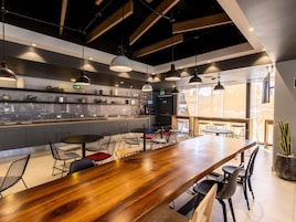Un restaurante moderno con una barra de madera larga, varias zonas de estar y vistas a la ciudad a través de las ventanas.