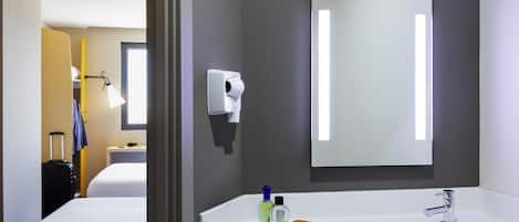 A hotel bathroom with a large mirror, a sink, and a toilet.