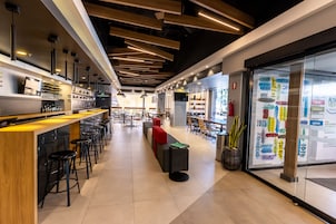 Un área de bar moderna con taburetes altos, una barra larga y un rincón de estar con un sofá rojo.