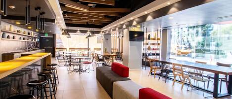 A modern restaurant interior with high ceilings, exposed beams, and a mix of bar and dining areas.