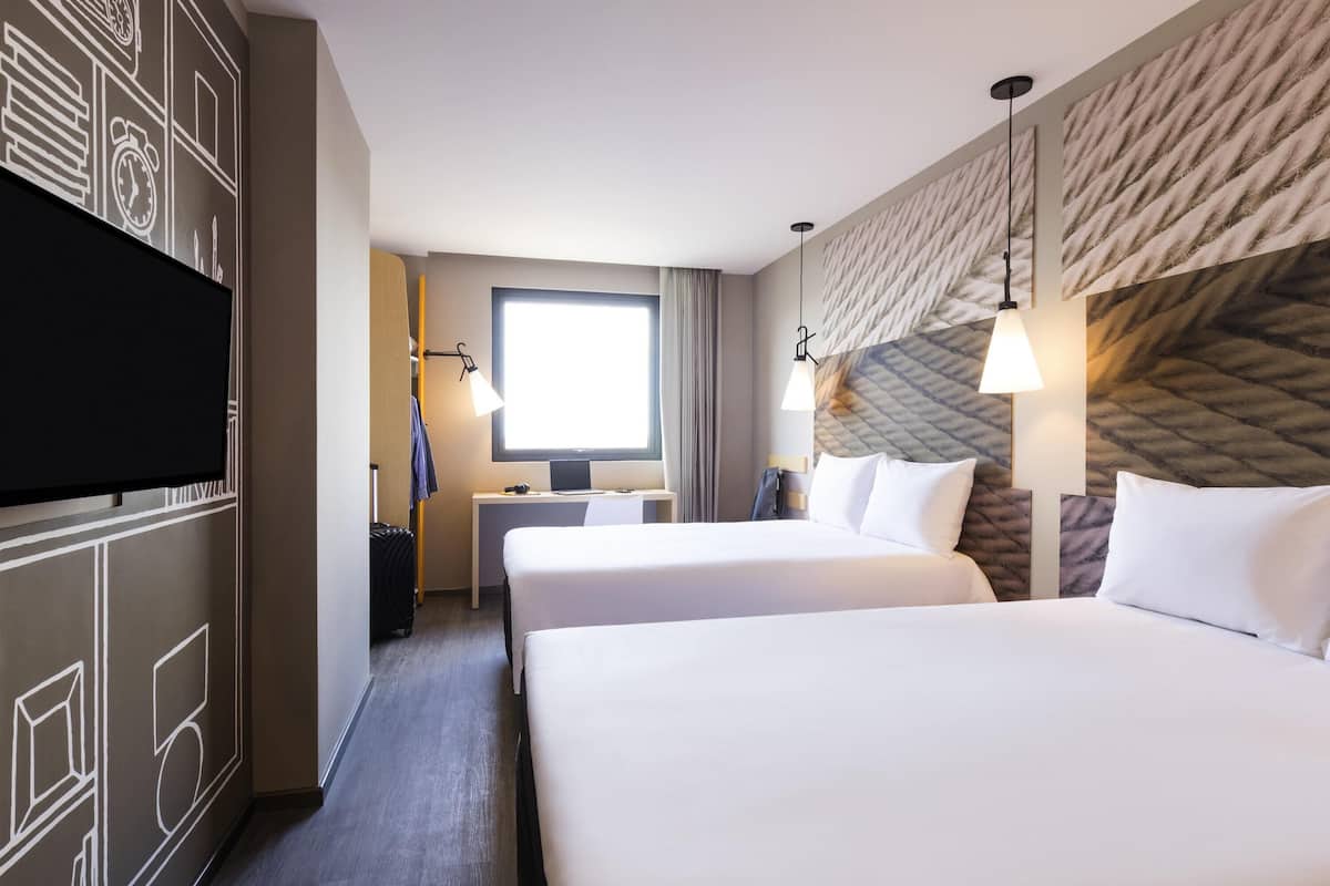 Habitación de hotel con dos camas, un escritorio, un televisor y una ventana con cortinas.