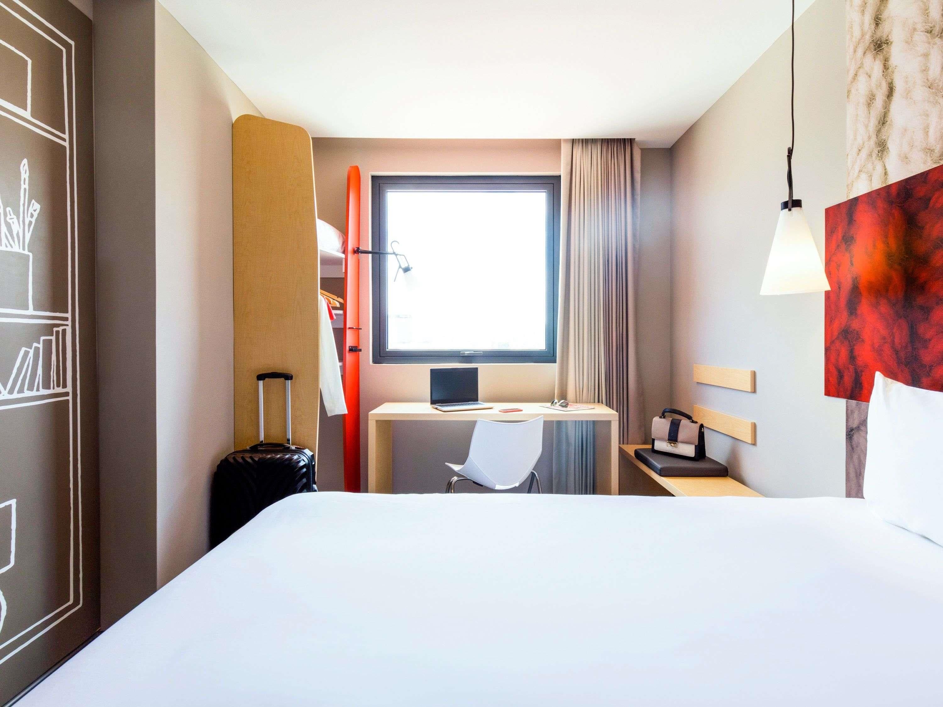 Una habitación de hotel con cama, escritorio, silla y maleta.