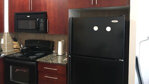 Una cocina con armarios de madera oscura, un microondas negro, una estufa negra y un refrigerador negro.