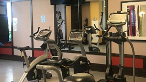 Un gimnasio con bicicletas estáticas, una cinta de correr y un espejo grande.