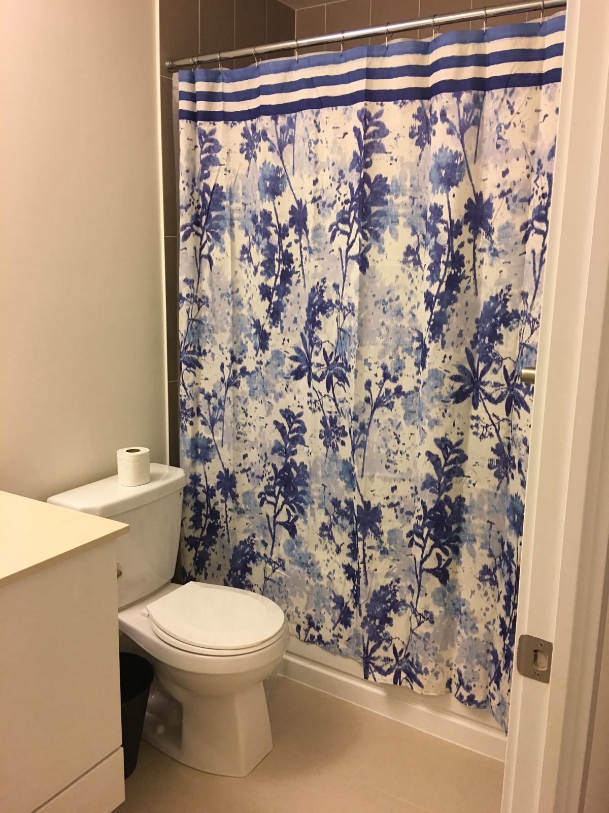 Un baño con inodoro, rollo de papel higiénico y cortina de ducha con estampado floral.