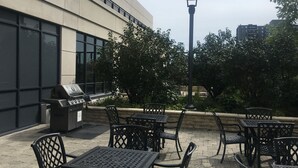Un patio al aire libre con mesas y sillas de metal, una parrilla y una farola.