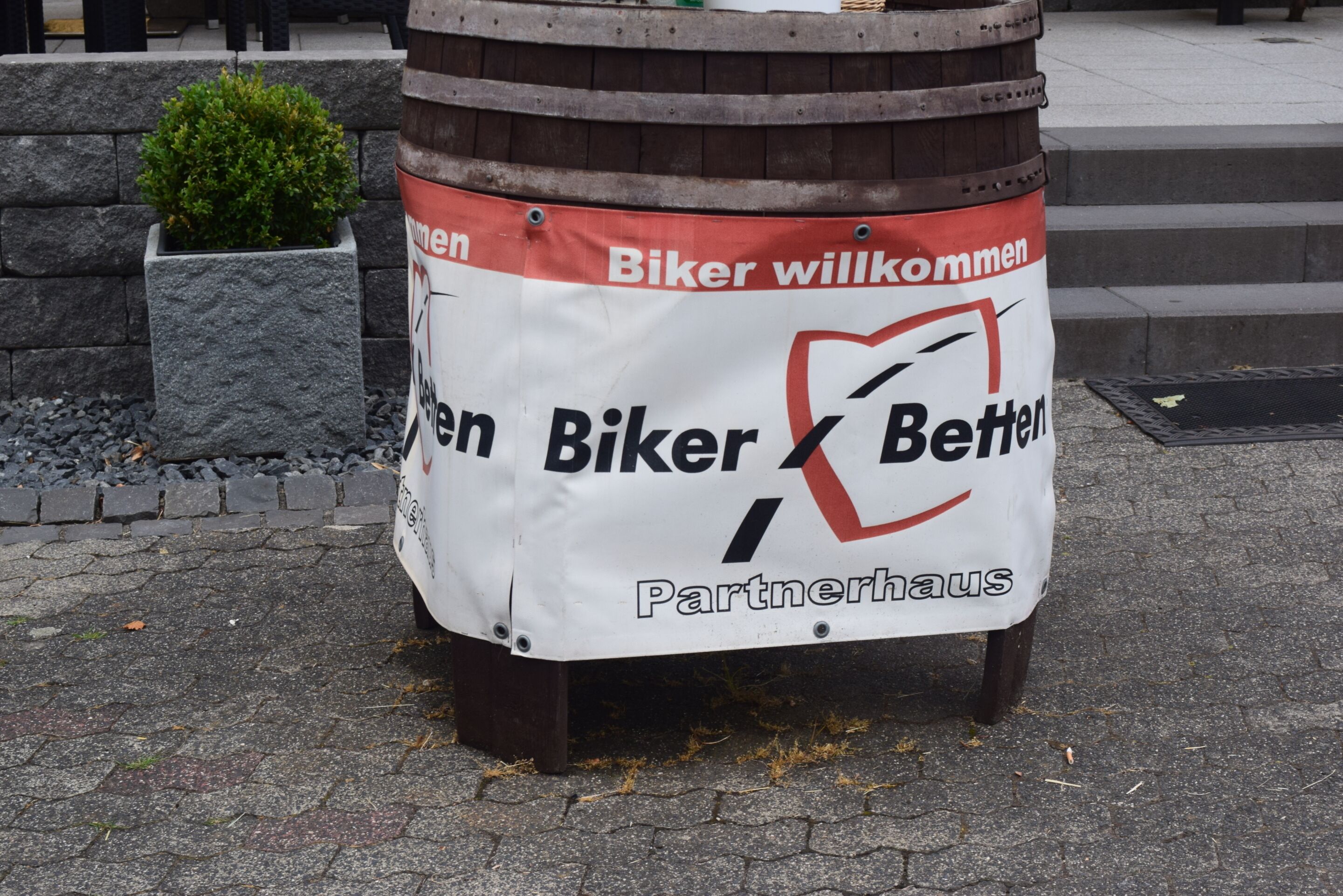 Ein Schild an einem Holzfass mit dem Text 'Biker willkommen' und 'Biker Better Partnerhaus'.