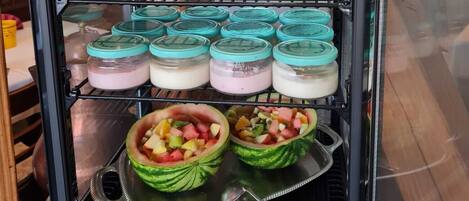 Un expositor de alimentos con varios frascos de comida y dos ensaladas de frutas en boles.