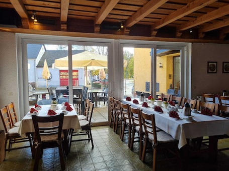 An indoor dining area with multiple tables and chairs, large windows, and a view of the outdoor patio area.