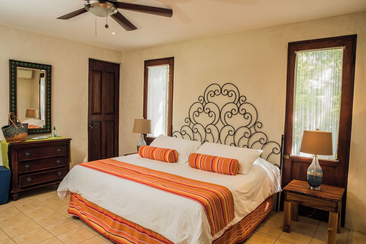 A bedroom with a bed, two bedside tables, a dresser, a ceiling fan, and a window with curtains.