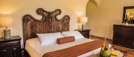 Una cama bien hecha con cabecera de madera, dos lámparas de noche, una mesita de noche con lámpara y una pequeña mesa con un adorno.
