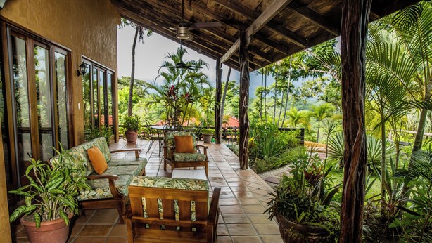 A covered outdoor seating area with wooden furniture and potted plants. - Hacienda Barrigona (Sámara)