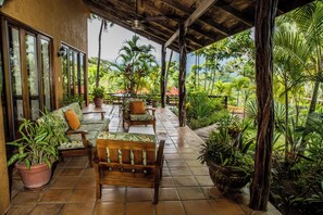 Uma área de estar ao ar livre coberta, com móveis de madeira e plantas em vasos.