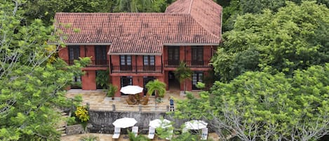 A large house with a tiled roof, surrounded by lush greenery and a swimming pool.