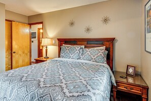 Une chambre à coucher avec un grand lit, une table de chevet en bois, une commode, une lampe et un certificat encadré accroché au mur.