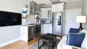 Una cucina compatta con elettrodomestici integrati, un'area pranzo con tavolo e sedie, e un soggiorno con divano e lampada.