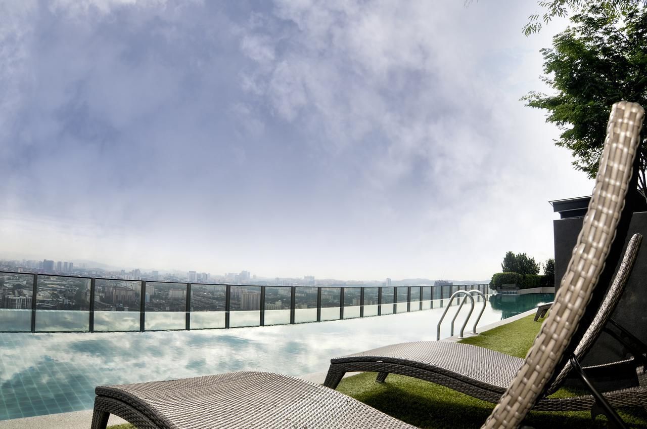 Una piscina infinita con vistas a la ciudad, sillas de descanso y barandilla de cristal.