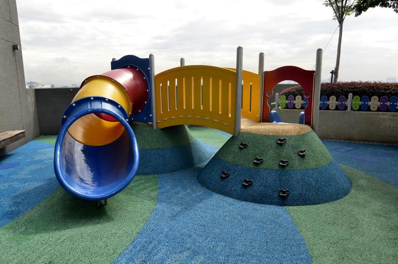 A children's play area with a slide, climbing structure, and soft play surface.