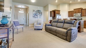 A spacious living room with a gray sofa, a white armchair, and a wooden coffee table. A kitchen with wooden cabinets and a microwave is visible in the background. - Private Pool, Mtn Views! Hurricane Group Getaway (Hurricane)