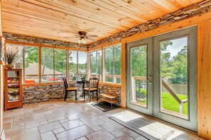 Relax in this serene outdoor space with a stone wall, ceiling fan, and glass doors offering a view of the surrounding landscape.