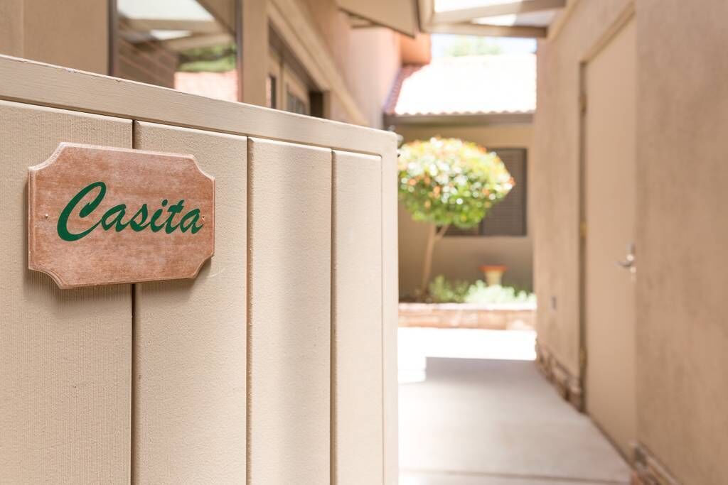 Ein hölzernes Schild mit der Aufschrift "Casita" an einer beigen Wand.