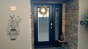 Une porte noire ornée d’une guirlande, une plaque avec l’inscription « Casa » et un élément décoratif en métal fixé au mur.