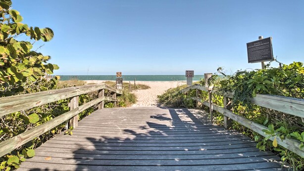 Ein Holzsteg führt zu einem Strand unter blauem Himmel.