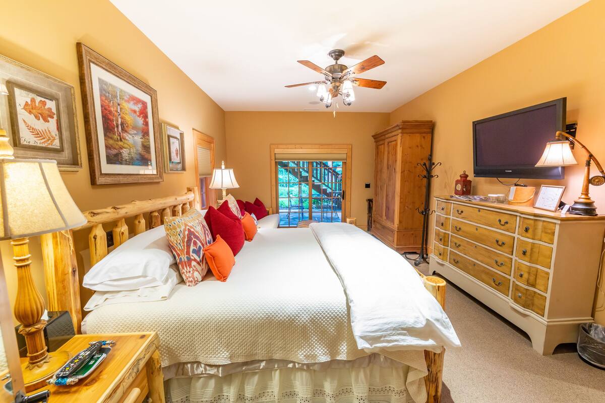 A bedroom with a large bed, a ceiling fan, a TV, and a wooden dresser.