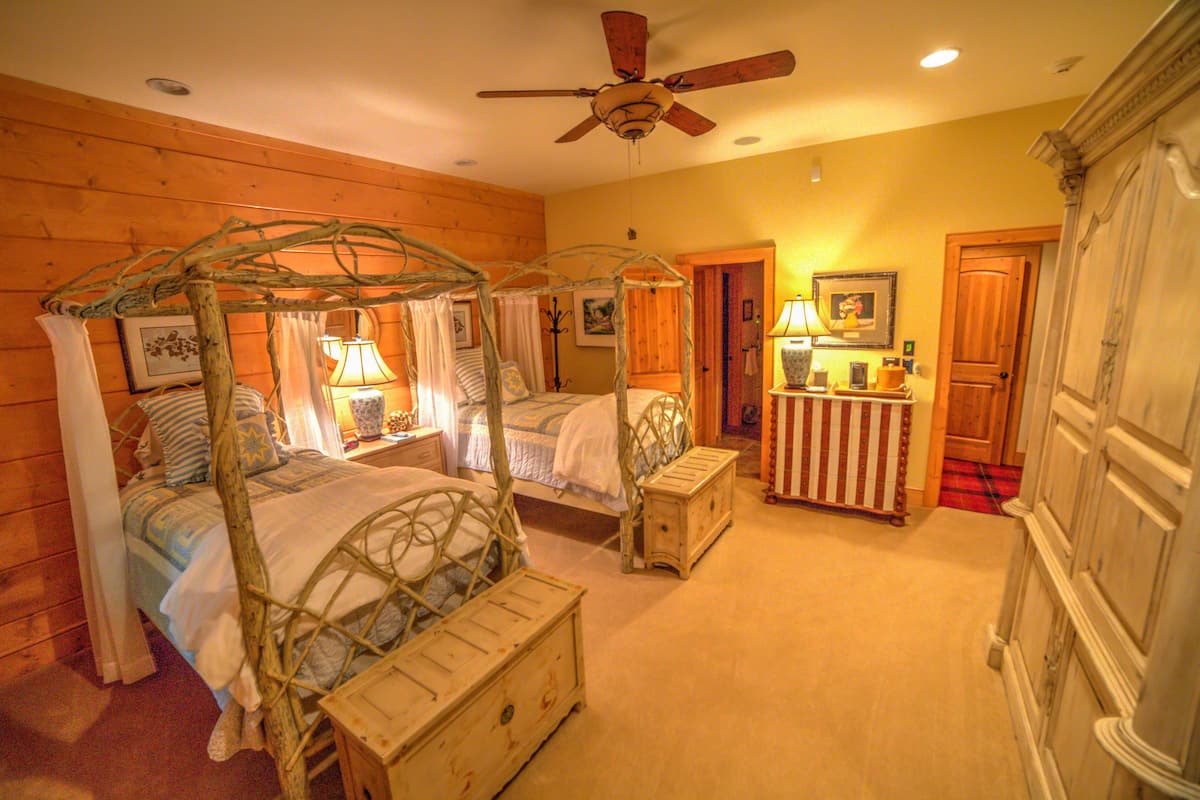 A bedroom with two four-poster beds, a wooden bench, a nightstand, and a dresser.