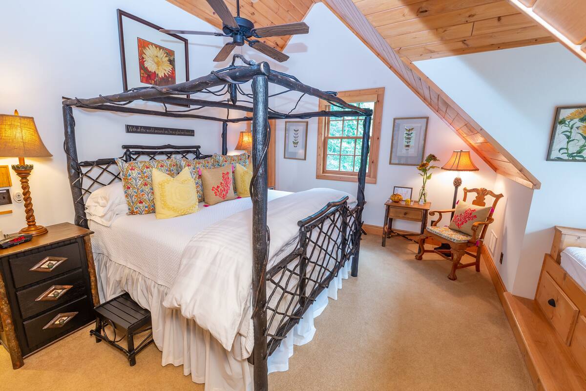 A four-poster bed with a wooden frame, a ceiling fan, and a view of the outdoors through a window.