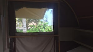 A room with a bed, a window with a view of greenery, and a curtain. - IDestinos Tayrona mobile home  (La Poza)