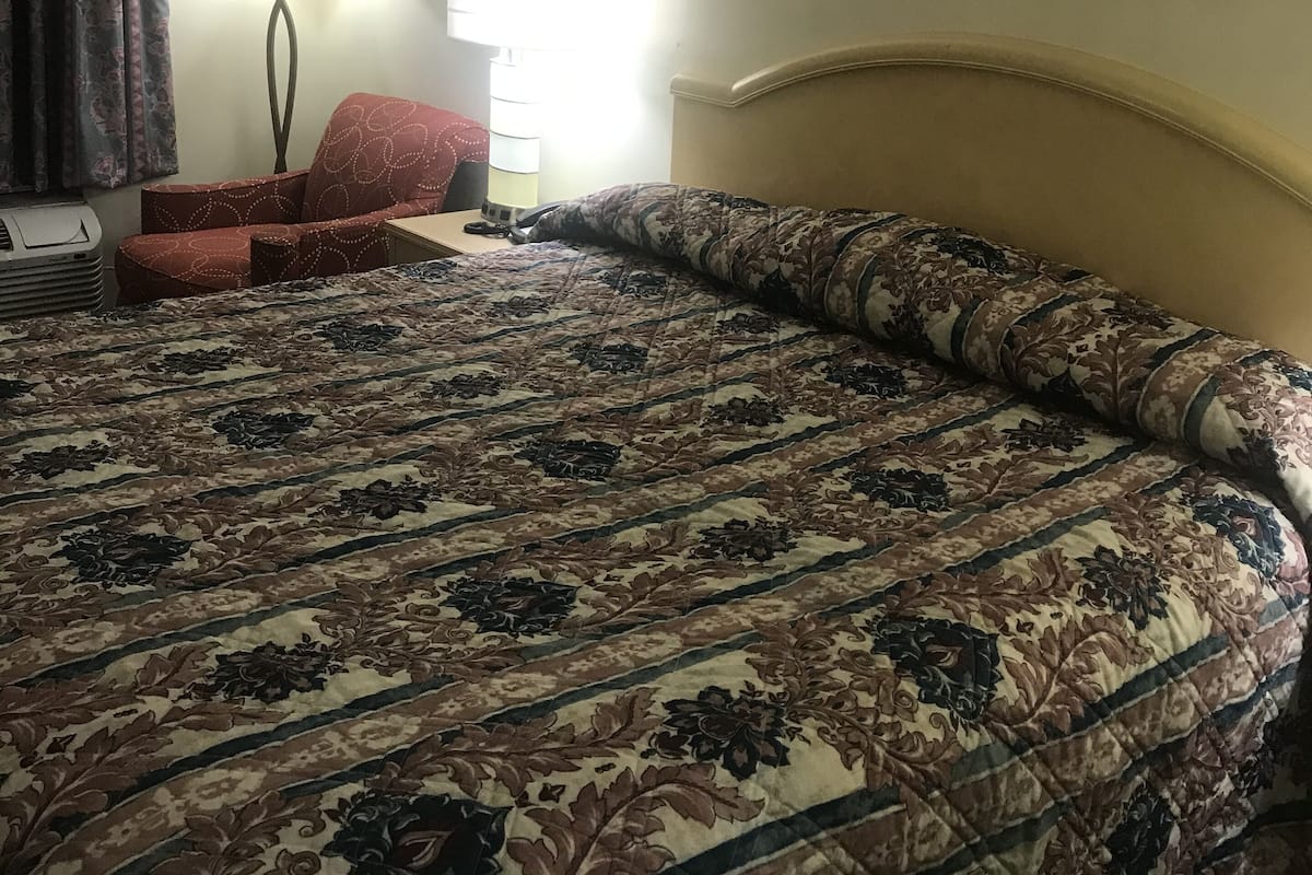 A hotel room with a large bed, a desk, a chair, a lamp, and two framed pictures on the wall.