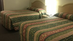 Ein Hotelzimmer mit zwei Betten, beide mit gemusterten Laken. Dazwischen steht ein Nachttisch mit einer Lampe.