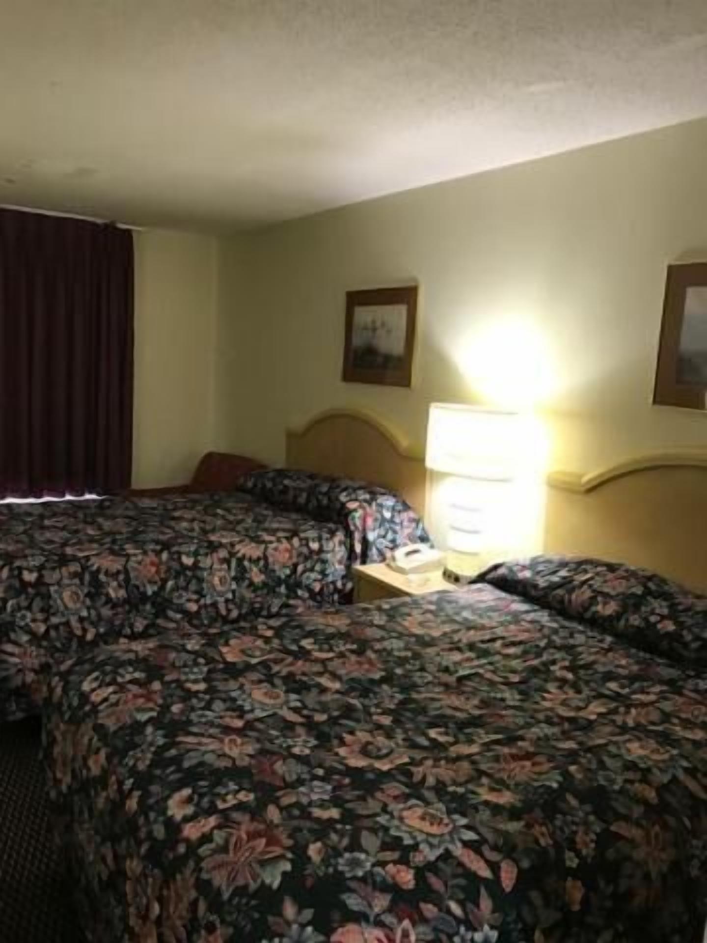 Una habitación de hotel con dos camas, una mesita de noche, una lámpara y un cuadro en la pared.