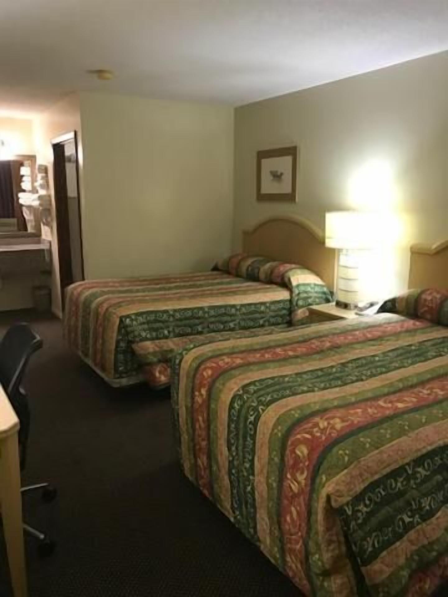 A hotel room with two beds, a desk, and a chair.
