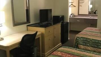 A hotel room with a desk, a television, a bed with patterned bedding, a dresser, and a mirror.