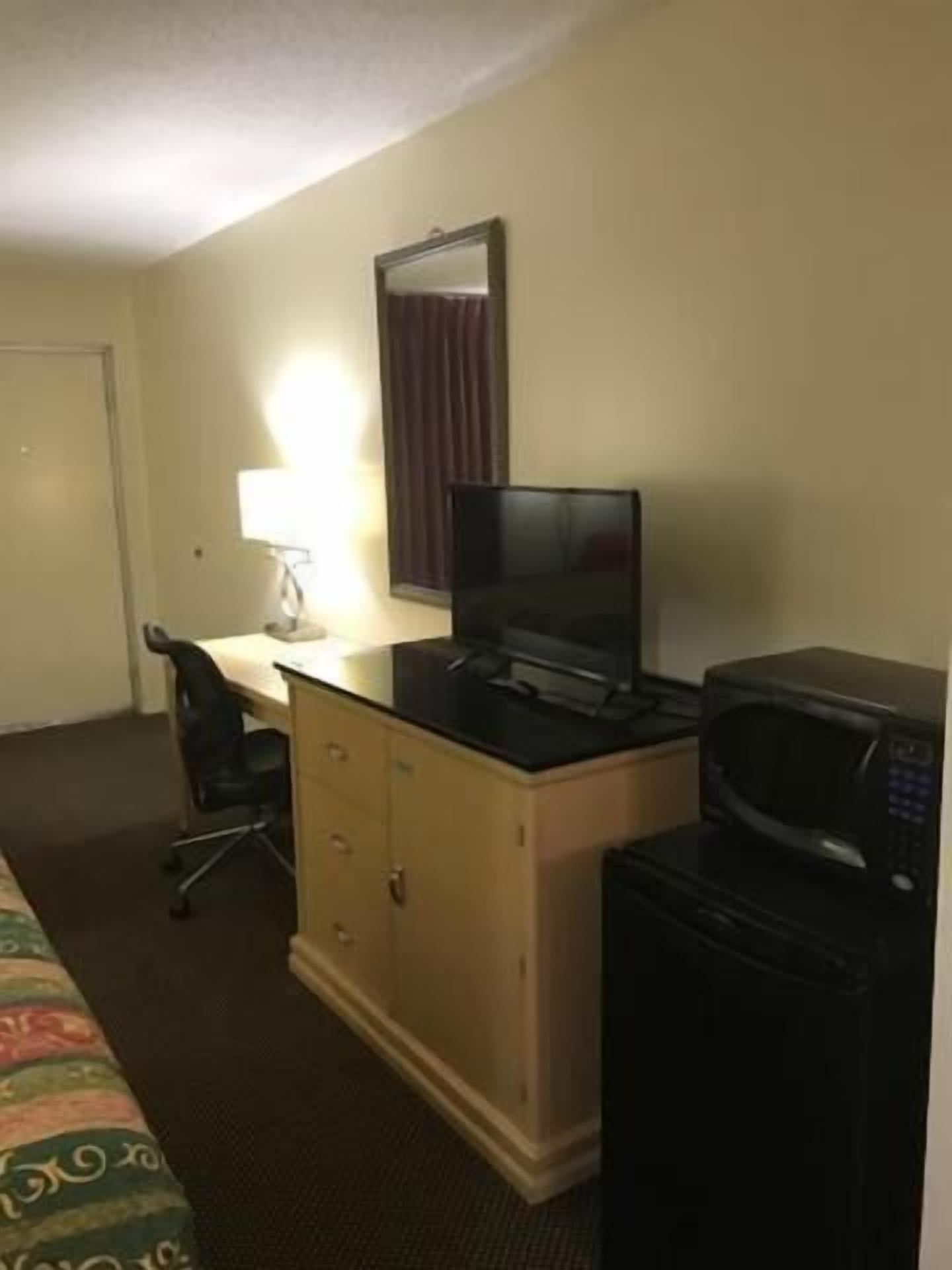 A hotel room with a bed, a desk with a computer, a microwave, and a TV.