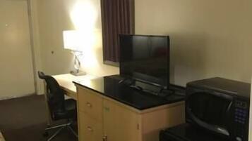 A hotel room with a bed, a desk with a computer, a microwave, and a TV.