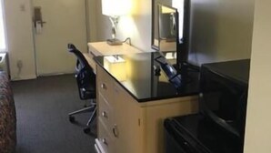 Ein Hotelzimmer mit einem Bett, einem Schreibtisch mit Lampe, einem Spiegel und einer schwarzen Mülleimer.