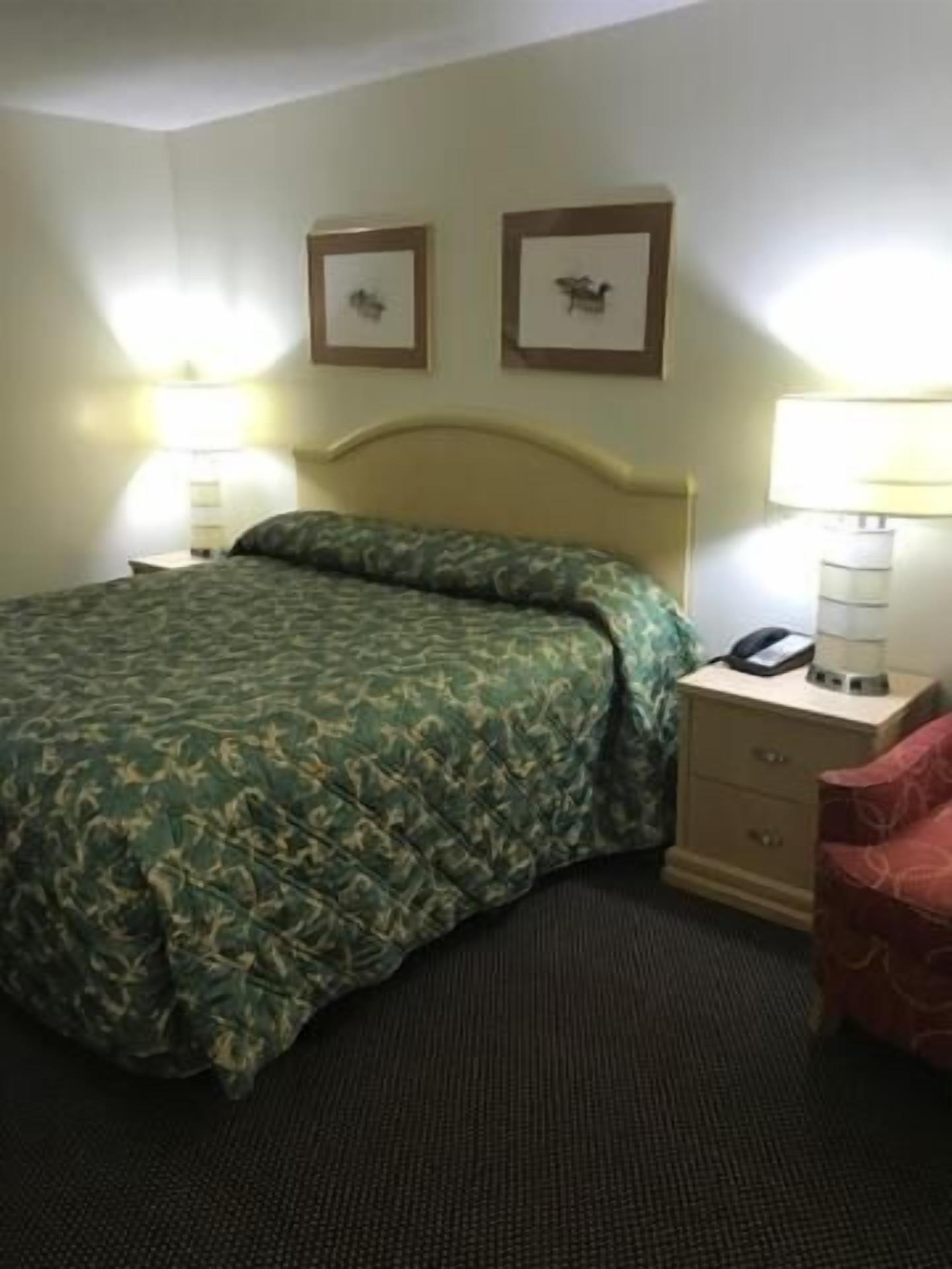 A hotel room with a bed, two bedside lamps, a nightstand with a phone, and two framed pictures on the wall.