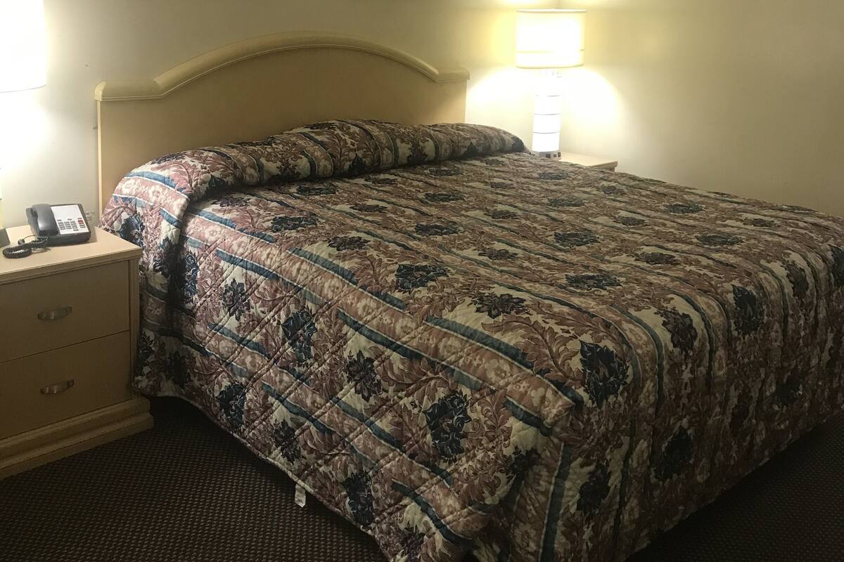 A hotel room with a bed, a bedside table with a phone, and two wall-mounted lamps.