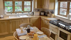 A kitchen with wooden cabinets, a stove, a sink, and a dining table set for breakfast. - 3 bedroom accommodation in Bacton, near North Walsham (Bacton, near North Walsham)