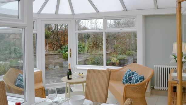 A conservatory with wicker furniture, a dining table set for two, and a view of the garden. - 3 bedroom accommodation in Bacton, near North Walsham (Bacton, near North Walsham)