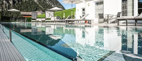 A swimming pool with lounge chairs and umbrellas, surrounded by a mountain landscape.