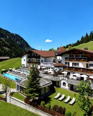 Un hotel con piscina, zona de estar al aire libre y montañas al fondo.