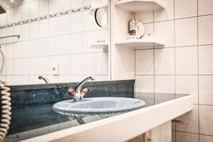 Un baño con lavamanos con cristal, un perchero y un espejo.